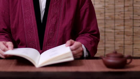 Front-view-of-an-Asian-man-reading-a-Chinese-book-in-a-traditional-robe,-faceless-person