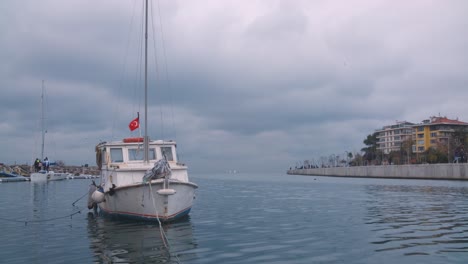 Boat-flying-a-Turkish-flag-docked-in-a-canal-on-a-cloudy-day,-close-view