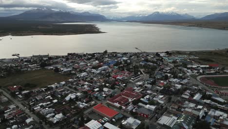 City-of-Puerto-Natales-Chile,-Aerial-Drone-Above-Town-Buildings-Amongst-Patagonian-Landscape-of-Idyllic-Bay-Water-and-Andean-Cordillera-Background