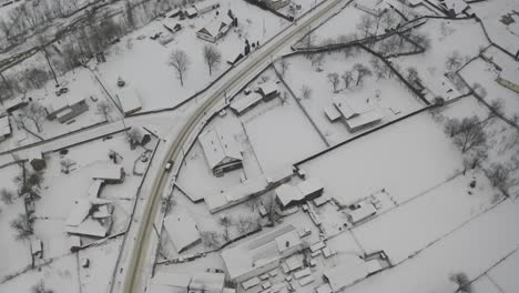 Drone-view-of-a-vehicle-driving-through-a-snow-covered-town