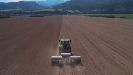 Tracking-aerial-shot-of-Tractor-flattening-vast-field-with-heavy-rollers