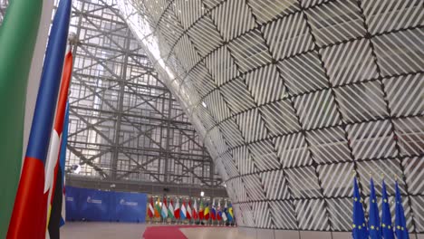 Looking-down-the-European-Council-building-with-EU-flags-and-national-country-flags-in-Brussels,-Belgium---Cinematic-tilt-down-shot