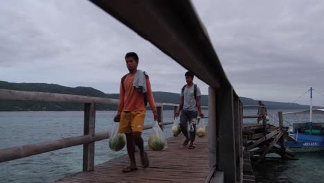 Lugareños-Filipinos-Caminando-Sobre-Un-Muelle-De-Madera-Transportando-Mercancías,-Desembarcados-De-Un-Barco-Atracado-En-La-Isla-Sumilon,-Cebu,-Filipinas