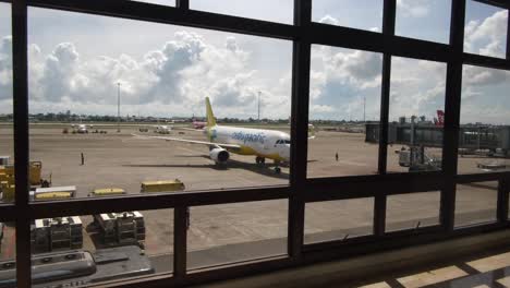 Passagiere,-Die-Tagsüber-Auf-Dem-Korridor-Des-Flughafens-Mit-Geparkten-Flugzeugen-Durch-Glasfenster-Laufen