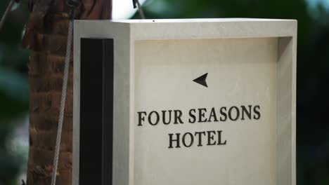 Welcome-to-the-Four-Seasons-Hotel---a-sign-pointing-to-the-left-next-to-a-tropical-palm-tree-trunk