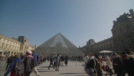 Wide-shot-of-the-louvre-glass-pyramid,-group-of-people-walking-by
