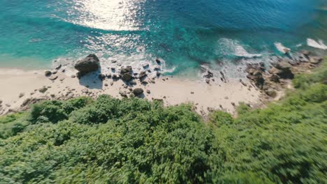 FPV-drone-horizontal-shot-of-majestic-cliffs-standing-tall-beside-coastline-with-waves-crashing-along-Suwehan-beach,-Nusa-Penida,-Bali-at-daytime