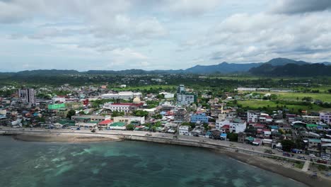 Establishing-Aerial-View-of-beachfront-rural-town-with-long-seawalls,-pristine-ocean-bays-and-mountainous-background-in-the-island-of-Catanduanes