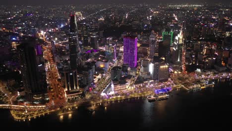 Ho-Chi-Minh-City,-Vietnam-iconic-Skyline-and-Saigon-river-waterfront-aerial-on-a-busy-night-featuring-all-key-buildings-illuminated-with-colored-lights