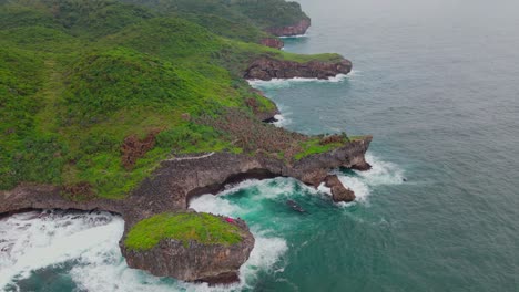 Aerial-footage-of-An-island-overgrown-with-dense-forest-with-coral-cliffs-and-big-waves