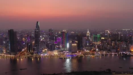 Ho-Chi-Minh-City,-Vietnam-iconic-Skyline-and-Saigon-river-waterfront-aerial-shot-on-a-busy-evening-featuring-all-key-buildings-illuminated-against-beautiful-colored-sky