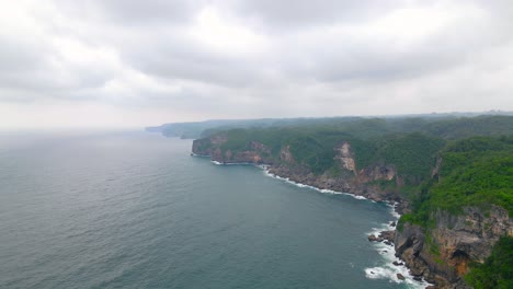 Vista-Aérea-De-La-Hermosa-Costa-Con-Paisaje-De-Selva-Verde-Durante-El-Día-De-Niebla-En-Indonesia