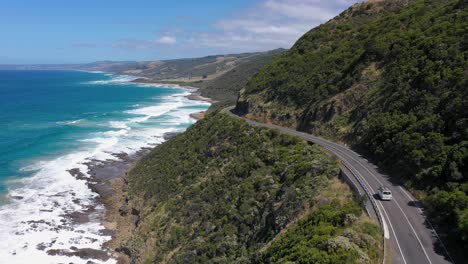 White-van-and-red-car-drive-along-Australia's-iconic-Great-Ocean-Road,-Victoria