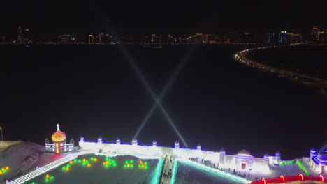Search-lights-sweep-night-sky-at-ice-festival-in-Harbin-China,-aerial