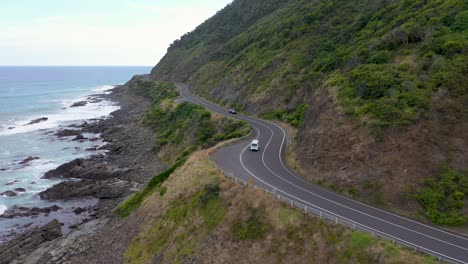 White-van-drives-on-curved-section-of-Great-Ocean-Road,-Victoria,-Australia
