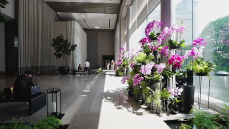 Die-Hotellobby-Ist-Mit-Natürlichem-Licht-Gefüllt,-Verfügt-über-Große-Fenster,-Die-Den-Raum-In-Warmes,-Sonniges-Tageslicht-Tauchen,-Und-Ist-Mit-Eleganten-Rosa-Orchideen-Geschmückt