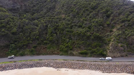 Car-with-caravan-driving-on-scenic-Great-Ocean-Road-side-view,-Victoria,-Australia