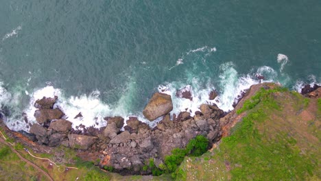 Overhead-drone-shot-of-cliffs-with-a-rocky-base-on-the-beach-hits-by-big-waves