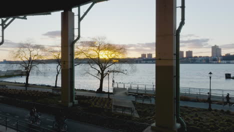 Aerial-view-through-the-Henry-Hudson-bike-trail,-towards-spring-sunrise-above-West-New-York