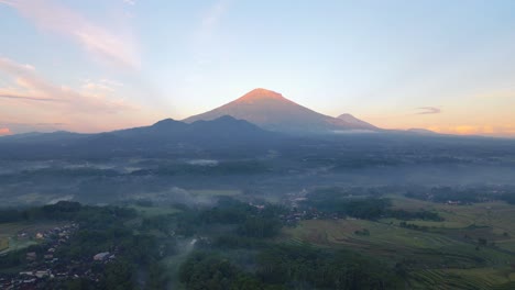 Aerial-footage-of-rural-landscape-with-view-of-countryside,-plantation-and-huge-mountain-in-the-morning-with-orange-sky