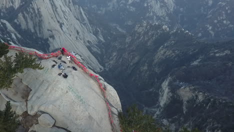 Aerial-tilts,-revealing-tourist-sitting-on-edge-of-steep-granite-cliff