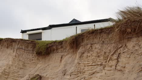 Coastal-erosion-of-Sandunes-on-Hemsby-Beach-with-house-on-the-Edge-of-a-cliff,-Mid-shot