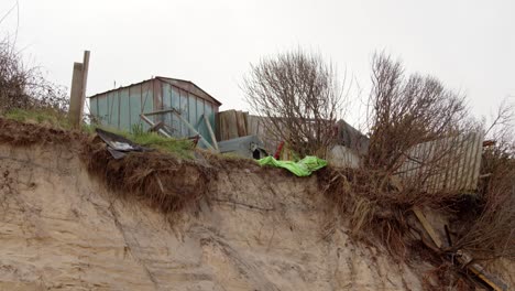 Coastal-erosion-of-Sandunes-on-Hemsby-Beach-with-garden-buildings-falling-over-the-edge-of-the-cliff,-Wide-shot