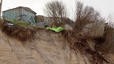 Coastal-erosion-of-Sandunes-on-Hemsby-Beach-with-garden-buildings-falling-over-the-Edge-of-the-cliff,-Wide-to-mid-shot