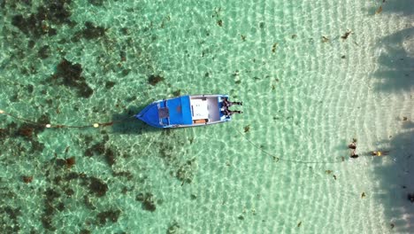 Bird-eye-drone-shot-of-docking-fishing-boat-near-the-shore-at-Anse-forbans-beach,-3-girls-playing-in-the-ocean,-Mahe-Seychelles