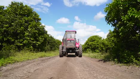 Slowmotion-low-angle-shot-of-a-tractor-driving-along-a-dirt-road-with-bushes