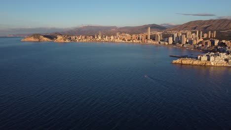 Aerial-ascending-view-of-bay-of-Benidorm-with-waterfront-skyscrapers-at-sunset-time