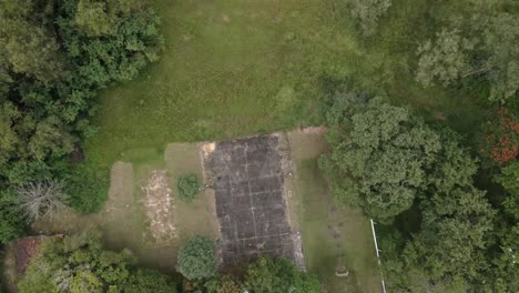 Abandoned-indoor-football-tennis-court-building-construction-among-bushes-and-trees-top-down-aerial-view