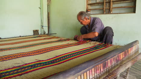 Asian-man-making-handmade-mattress,-cutting-loose-strands-from-the-rug