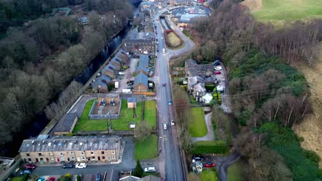 Drone-shot-of-the-peaceful-english-town,-showing-a-main-road-with-the-canal-running-along-side-it,-in-the-scenic-town-of-todmorden-in-northwest-yorkshire