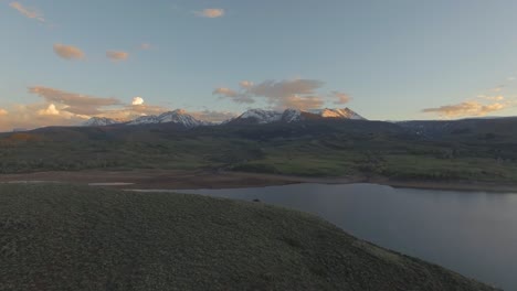 Wunderschöner-Sonnenuntergang-Mit-Boom-Schwenkaufnahme-über-Berghang-In-Schneebedeckten-Felsigen-Bergen-Und-See