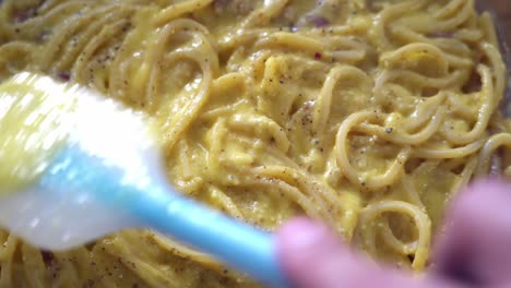 Kitchen-spatula-brushes-over-freshly-made-spaghetti-carbonara,-close-up