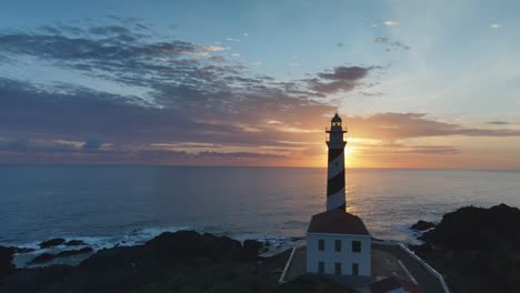 Silhouette-Des-Leuchtturms-Mit-Sonne,-Die-Bei-Sonnenuntergang-Hinter-Dem-Turm-Auf-Menorca,-Spanien,-Späht