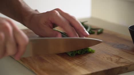 Professional-chef-chopping-spring-onions-on-a-wooden-cutting-board,-medium-shot
