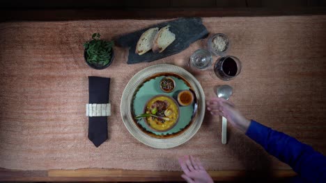 overhead-shot-of-a-woman's-hands-putting-a-plate-with-food-on-a-rustic-style-served-table