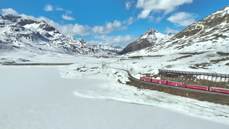Long-red-train-driving-over-a-railway-track-in-a-winters-landscape-in-Switzerland