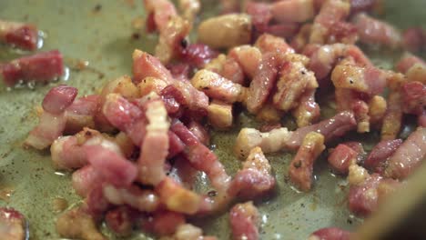 Fat-and-unhealthy-bacon-frying-in-pan,-wooden-spoon-stirring,-extreme-close-up