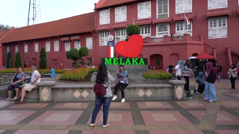 Tourists-take-photos-at-this-iconic-historic-Dutch-Square-against-maroon-coloured-structures-in-the-colonial-style-in-Malacca-,-Malaysia