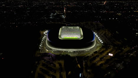 Aerial-view-away-from-the-BBVA-stadium,-night-in-Monterrey,-Mexico---reverse,-tilt,-drone-shot