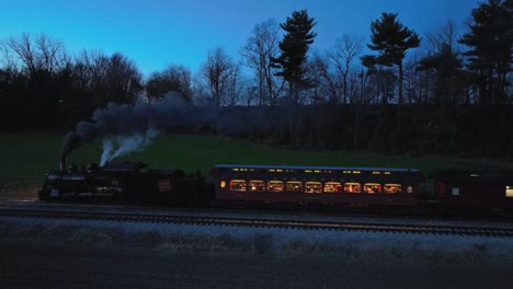 A-Drone-Parallel-Night-View-of-a-Steam-Passenger-Train-Slowing-Traveling-Thru-Farmlands-Seeing-the-Lights-in-the-Coaches