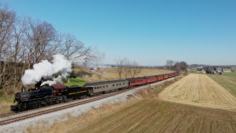 A-Drone-View-of-an-Antique-Steam-Passenger-Train,-Approaching,-Blowing-Smoke,-While-Traveling-Thru-Farmlands,-on-a-Sunny-Fall-Day