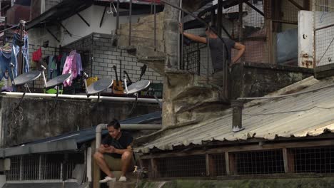 Ein-Mann-Sitzt-Auf-Der-Treppe-Und-Scrollt-Auf-Seinem-Handy,-Während-Er-Mit-Seinem-Freund-In-Kuala-Lumpur,-Malaysia,-Plaudert