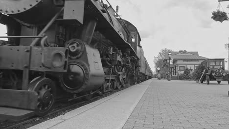 Eine-Schwarz-Weiß-Ansicht-Eines-Antiken-Dampfzugs-Mit-Niedrigem-Kamerawinkel,-Der-In-Einem-Bahnhof-Ankommt-Und-An-Einem-Wintertag-Rauch-Ausströmt
