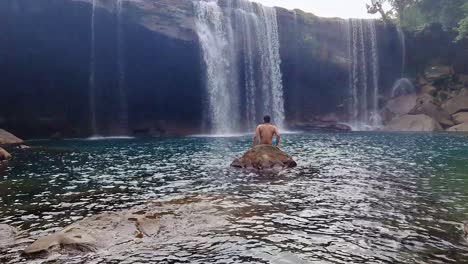 Mann-Genießt-Natürlichen-Wasserfall-Am-Morgen-Aus-Flachem-Winkel