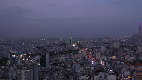 Ho-Chi-Minh-City,-Vietnam-evening-featuring-canal,-landmark-building-and-view-over-rooftops-to-urban-sprawl-and-main-road-under-lights