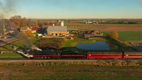 Drohnen-Parallelansicht-Einer-Dampfmaschine,-Die-Viel-Rauch-Ausbläst-Und-Am-Frühen-Morgen-Rückwärts-Fährt,-Während-Sie-Durch-Das-Ackerland-Fährt